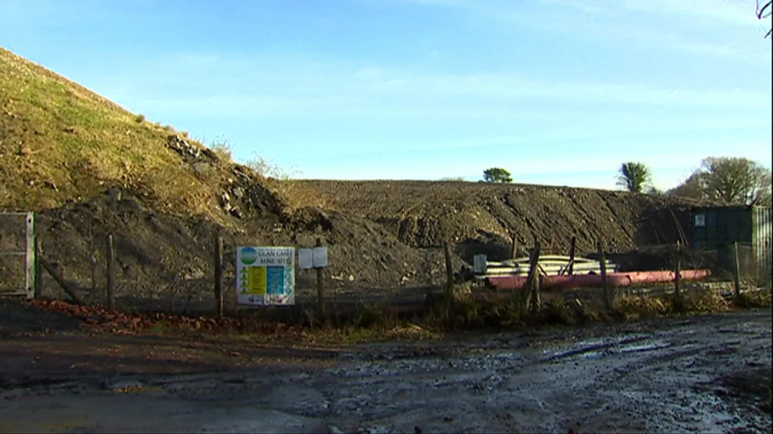 Glan Lash opencast mining site in Llandybie, Carmarthenshire. A mound of land can be seen behind a metal fence with the entrance sign on.