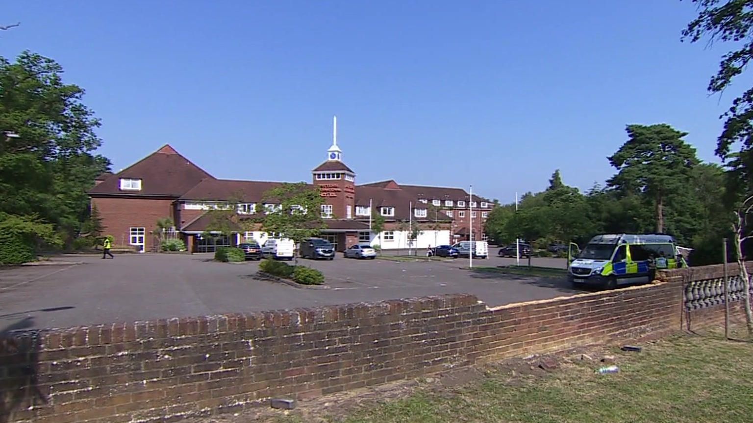 Exterior view of red brick hotel with car park in front. Police van is parked in the car park.