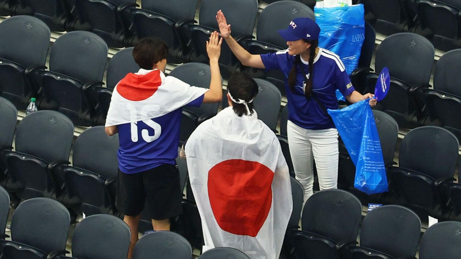 美国德州阿灵顿达拉斯球场FIFA世界杯F组日本对荷兰赛事结束后，一名帮忙打扫的日本女球迷（右）跟一名身披日本国旗的男球迷（左）击掌（14/6/2026）