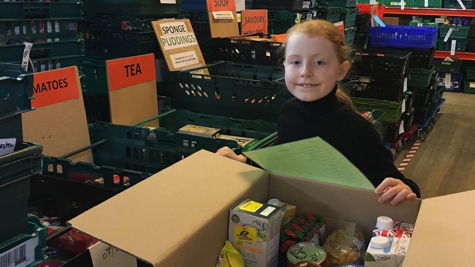 Image of Luna volunteering at the food bank. She is packing items into a cardboard box
