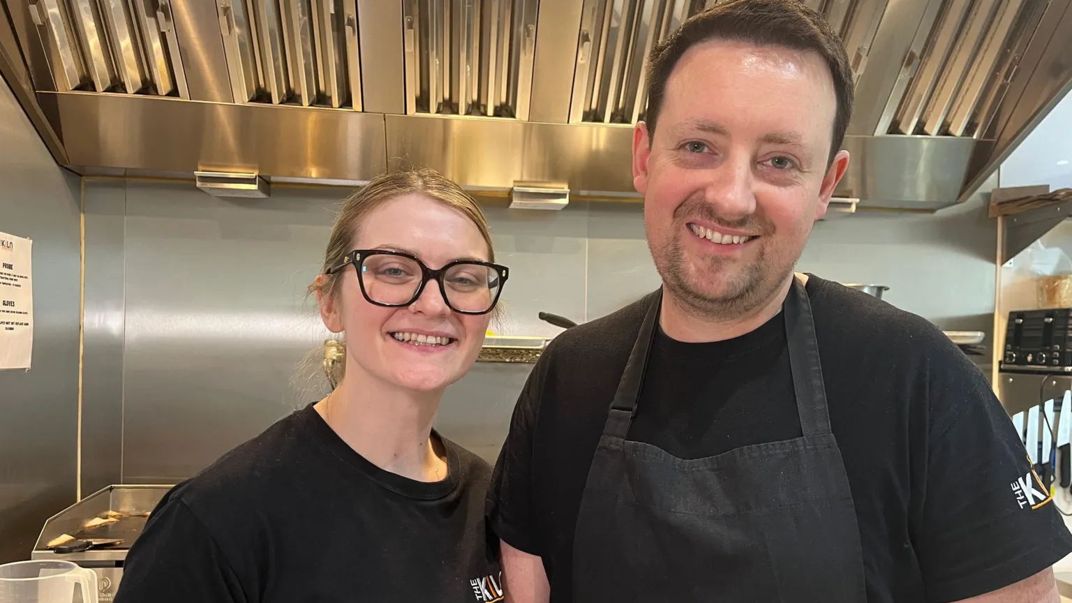 Nicola Haseler/BBC Two people dressed in black, smiling in a silver kitchen.