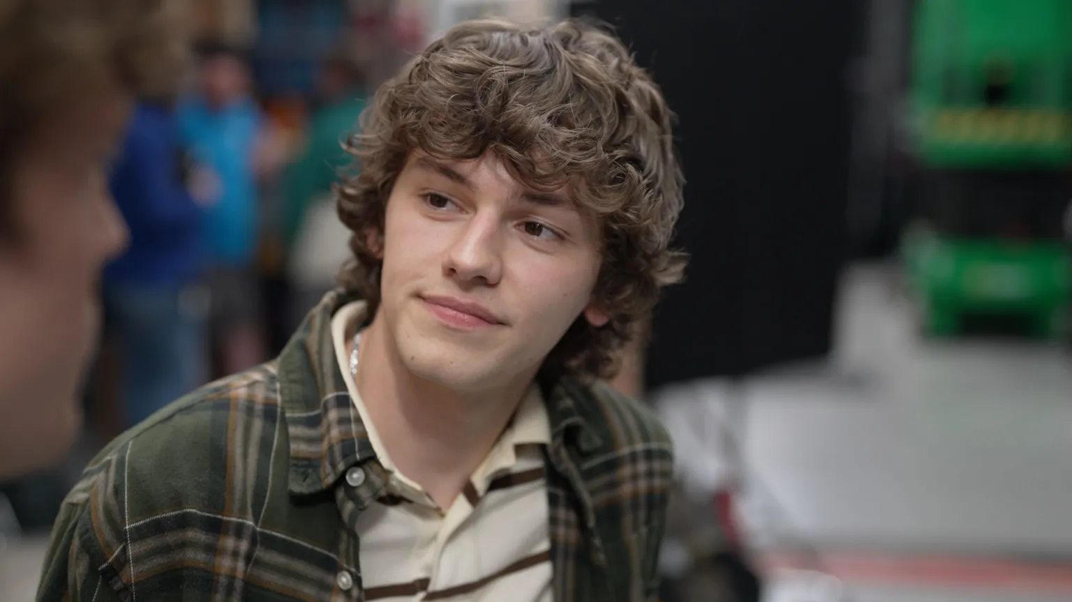 Ann Gannon / BBC News Actor Jackson Connor, who has curly hair and wears a plaid shirt over a striped polo shirt, looks off camera towards his co-star, who is out of vision.