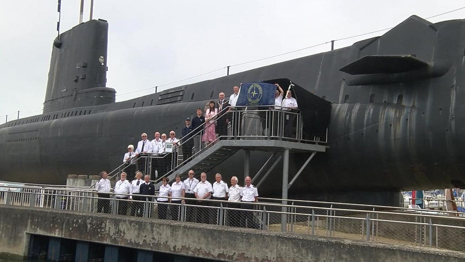 NCI staff outside a submarine holding the blue and gold NCI flag