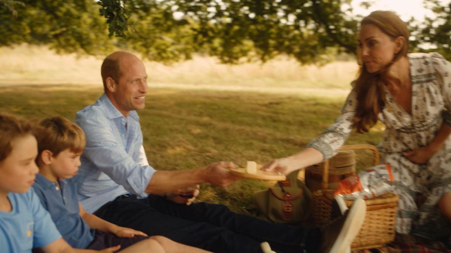 Princes Louis and George sit alongside their father on a picnic blanket as Kate hands over a cheese board