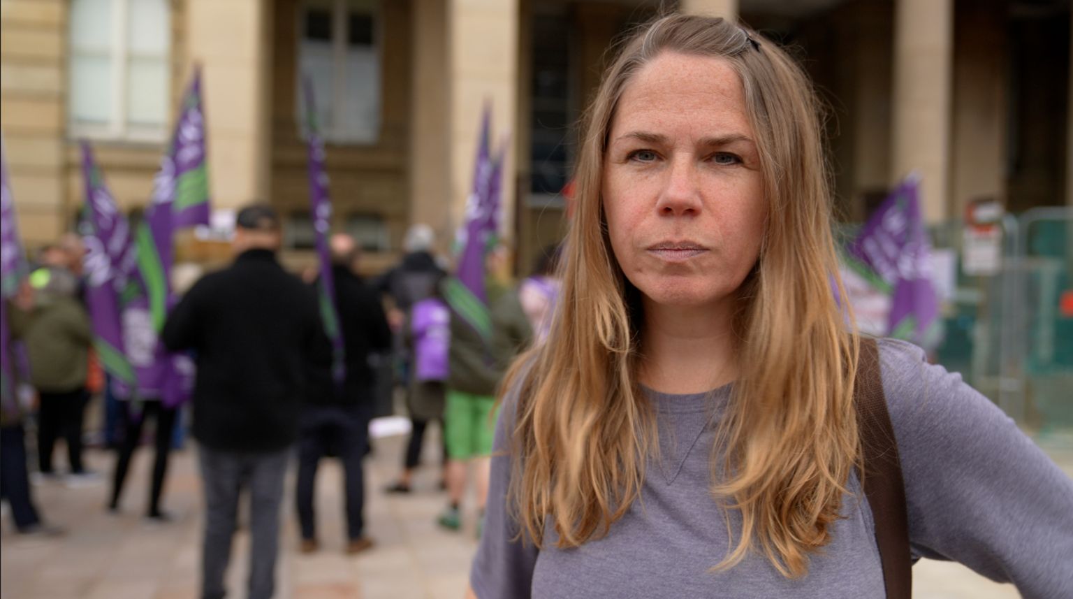 Kate Taylor, organiser of campaign group Brum Rise Up, standing in front of fellow protesters, some holding flags, demonstrating against cuts to services