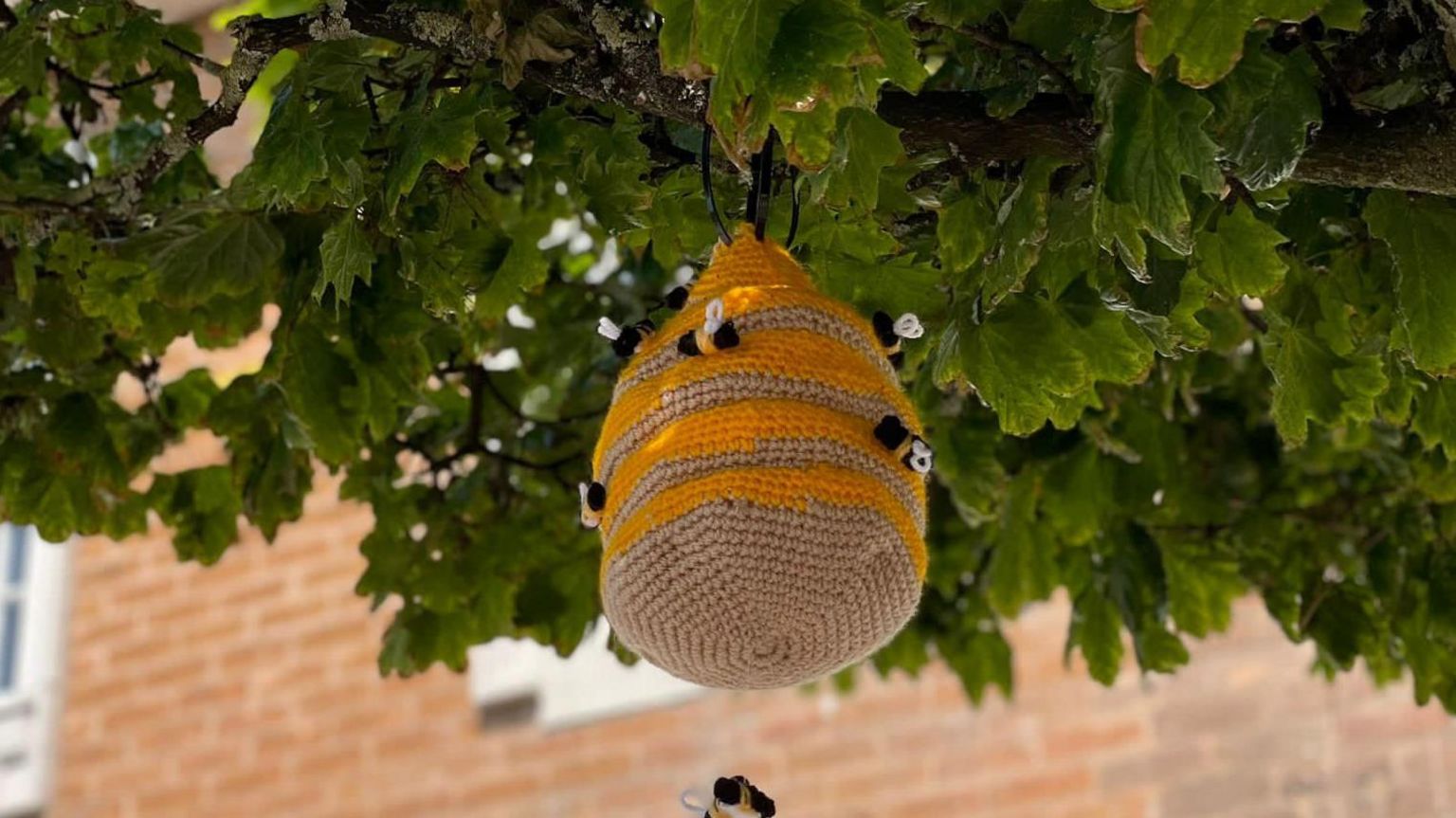 A knitted beehive hangs from a tree