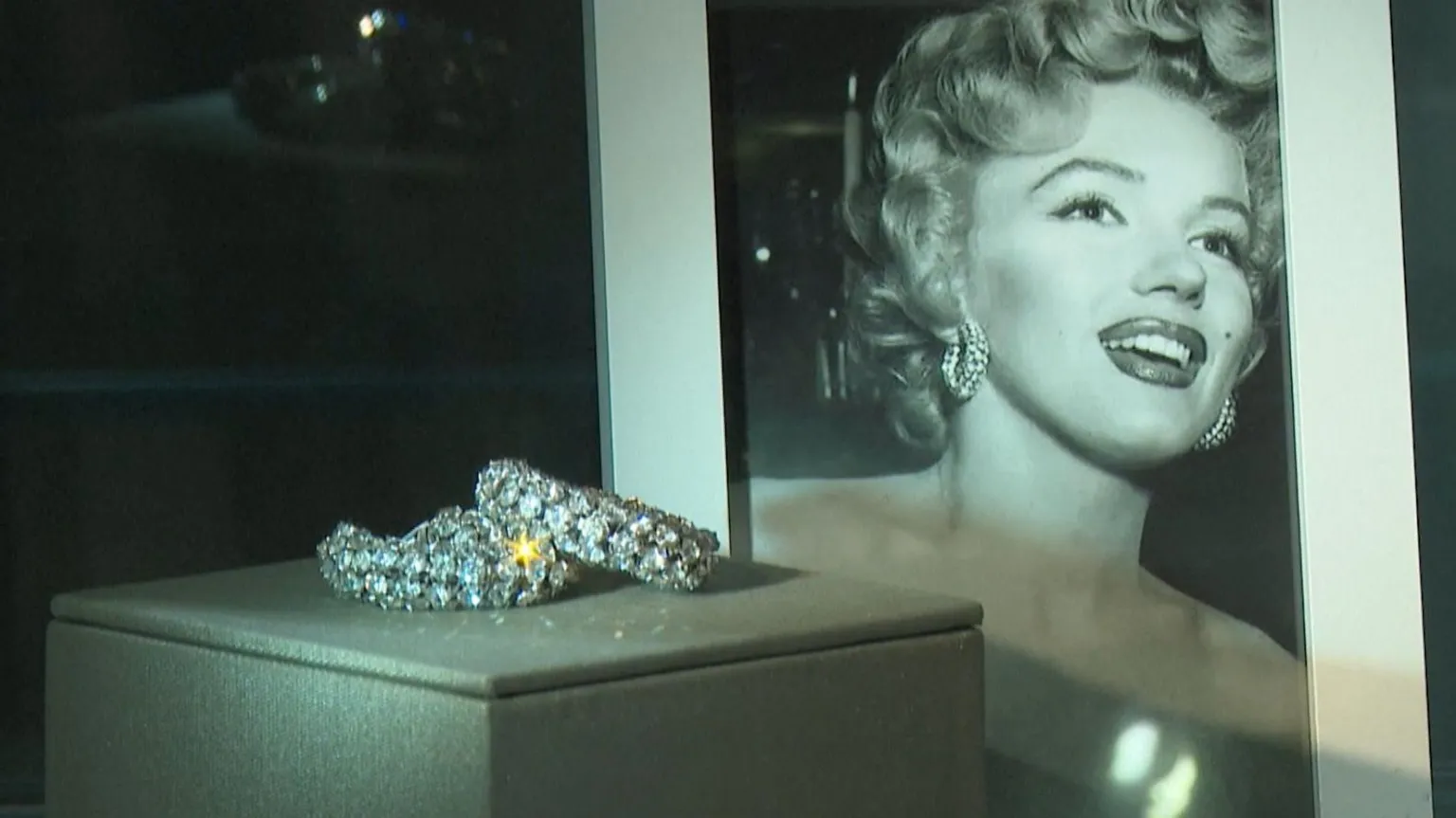 Sparkling earrings sit in a glass case in front of a portrait of Marilyn Monroe