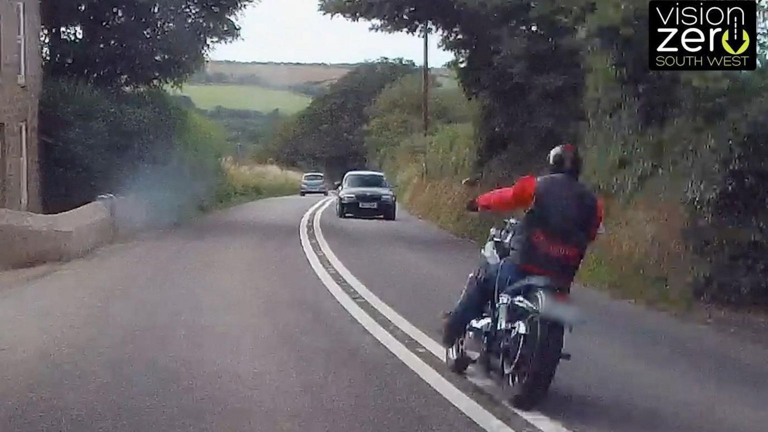 A motorcyclist on the wrong side of the road after crossing a solid white line, facing an oncoming car