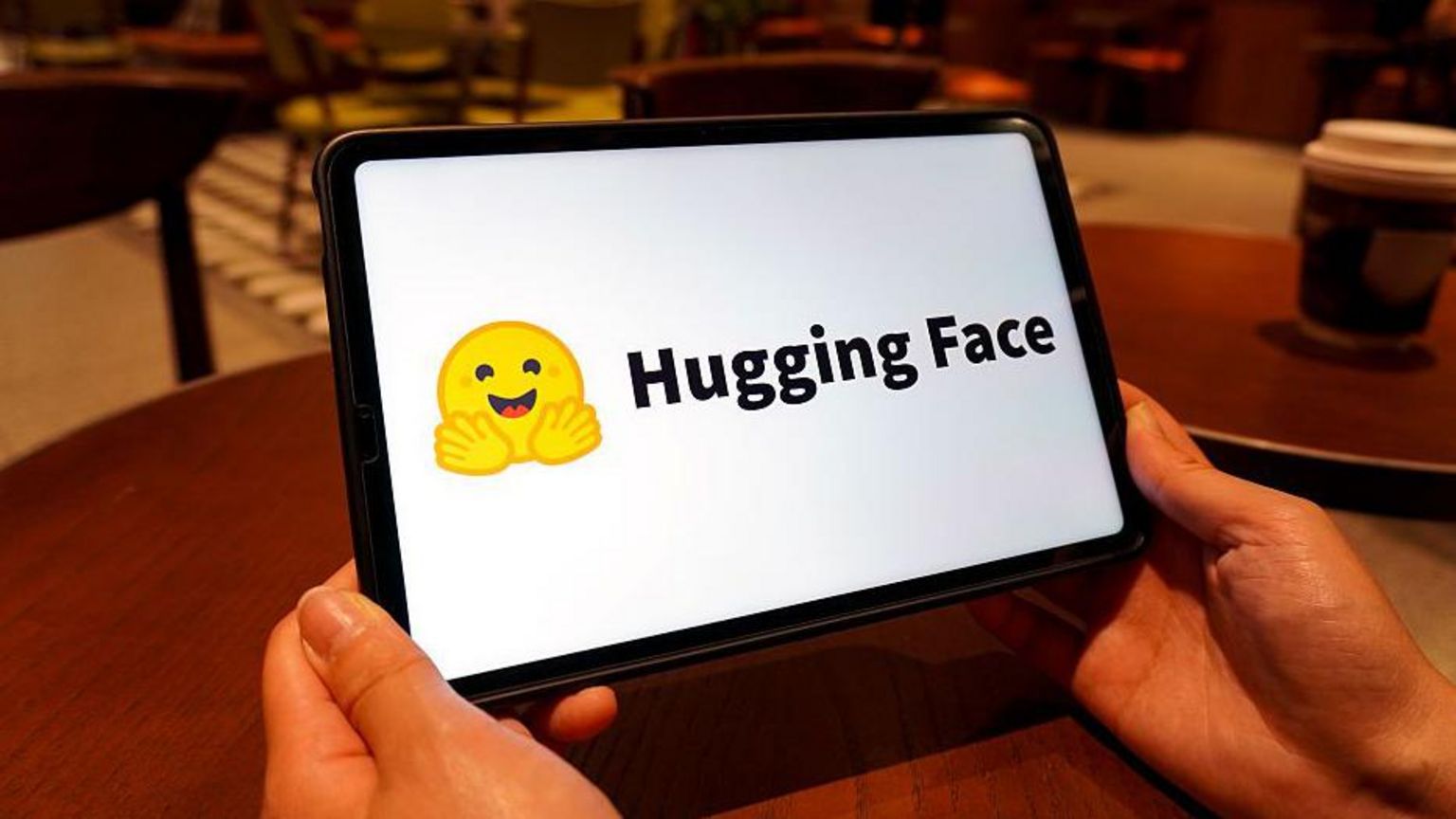 Hugging Face标志显示于平板电脑萤幕上。该标志是一个黄色笑脸表情符号，双手向前张开。