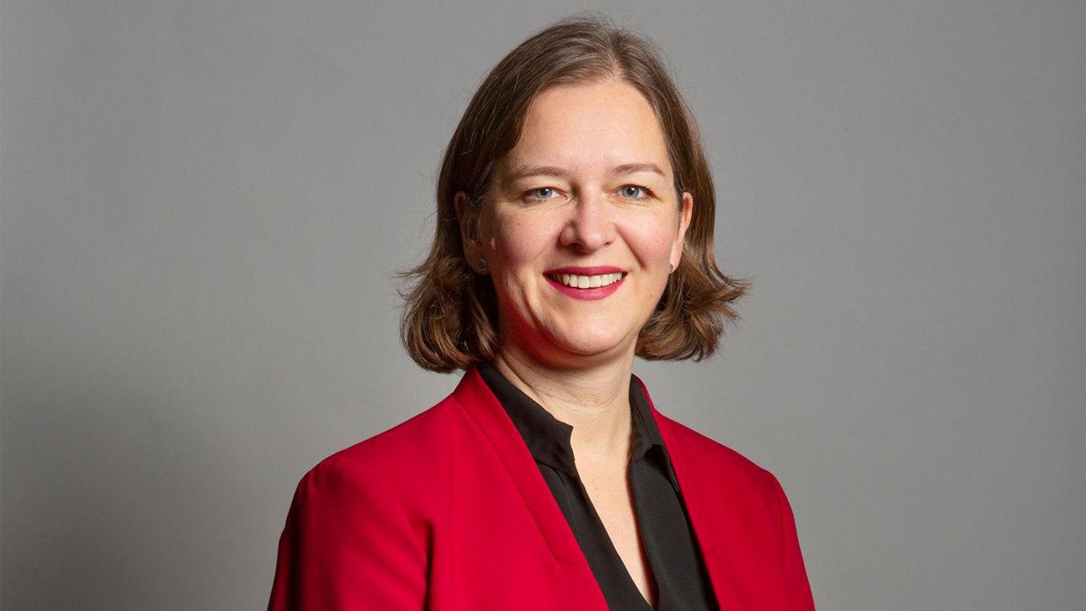 Fleur Anderson, wearing a red blazer and black top. She has chin length brown hair and is smiling.