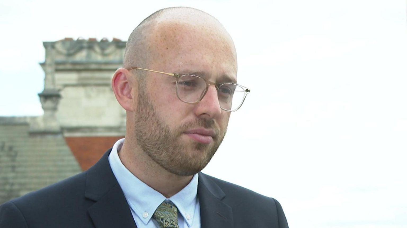 Lloyd Hatton, a bald man with a beard and glasses wearing a suit and tie.