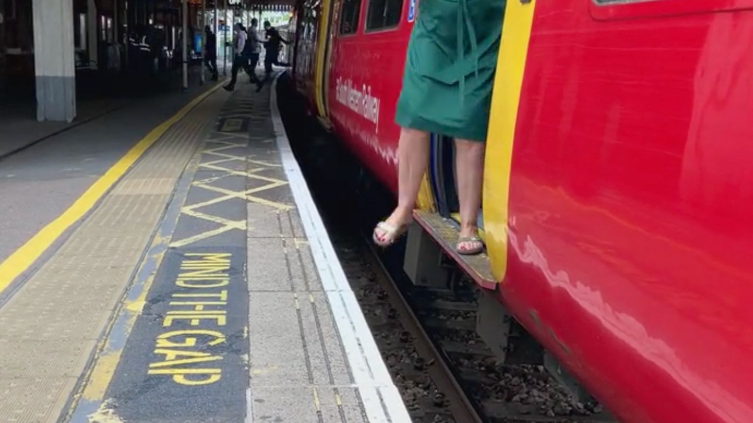 A woman stepping off the train carriage to the platform where there is a large gap - both in height and distance. The platform has a Mind the Gap signage painted on the floor.