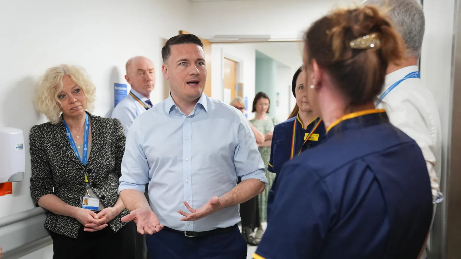 PA Wes Streeting, in a blue shirt, stands in a hospital corridor speaking to staff.