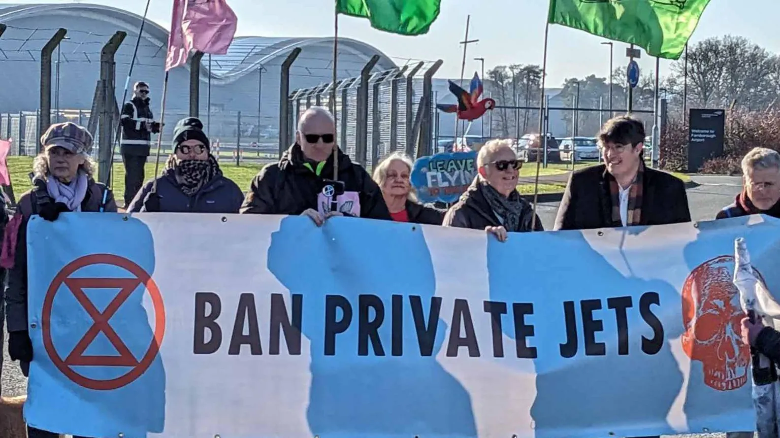 The image shows environmental protesters holding a large blue and white banner reading 