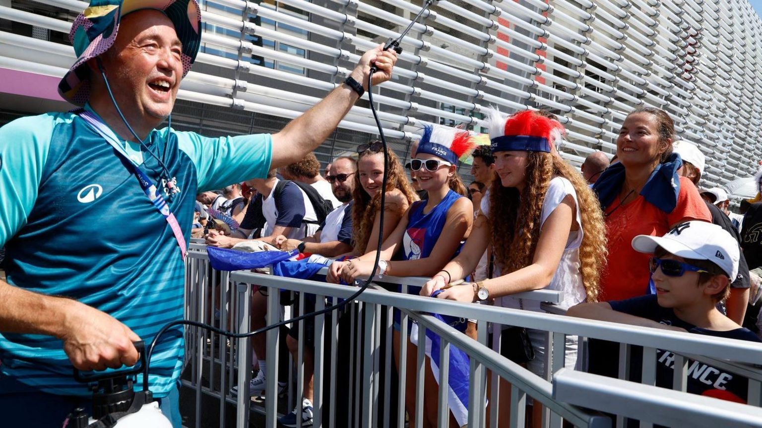 A volunteer sprays fans with water to cool them down