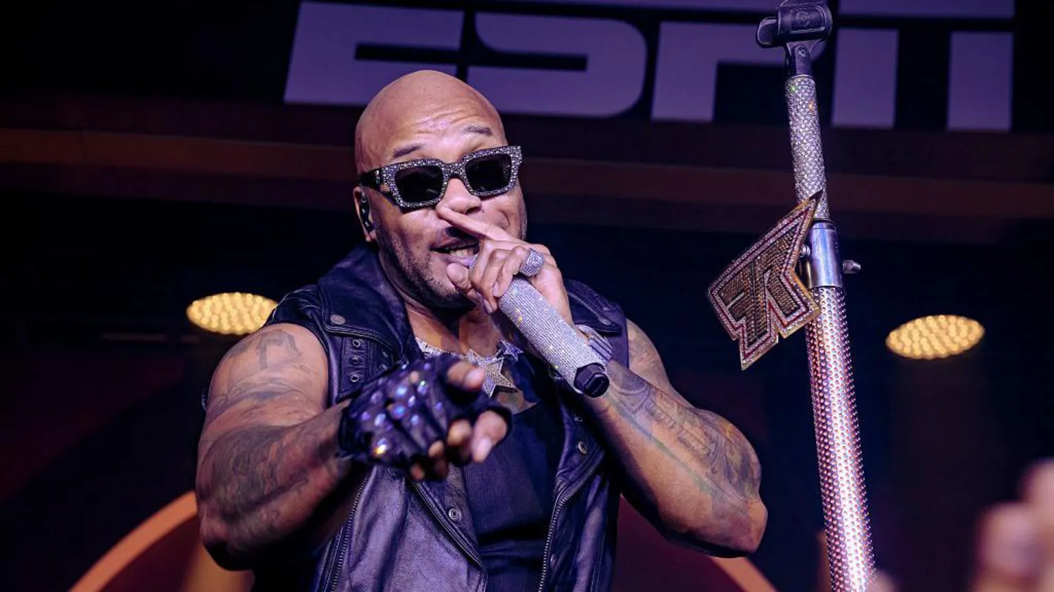 Getty Images A man wearing rhinestone-studded sunglasses sings into a rhinestone studded microphone while he points with his right hand