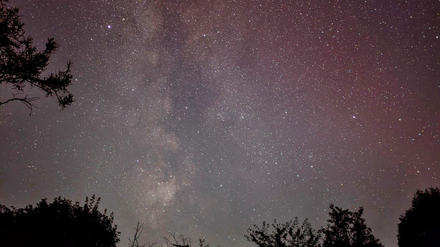 A night sky filled with stars and a soft red glow in the Cotswolds