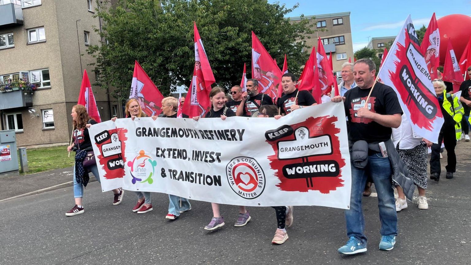 People marching with a large rectangular banner, reading 'Grangemouth refinery extend, invest and transition' 