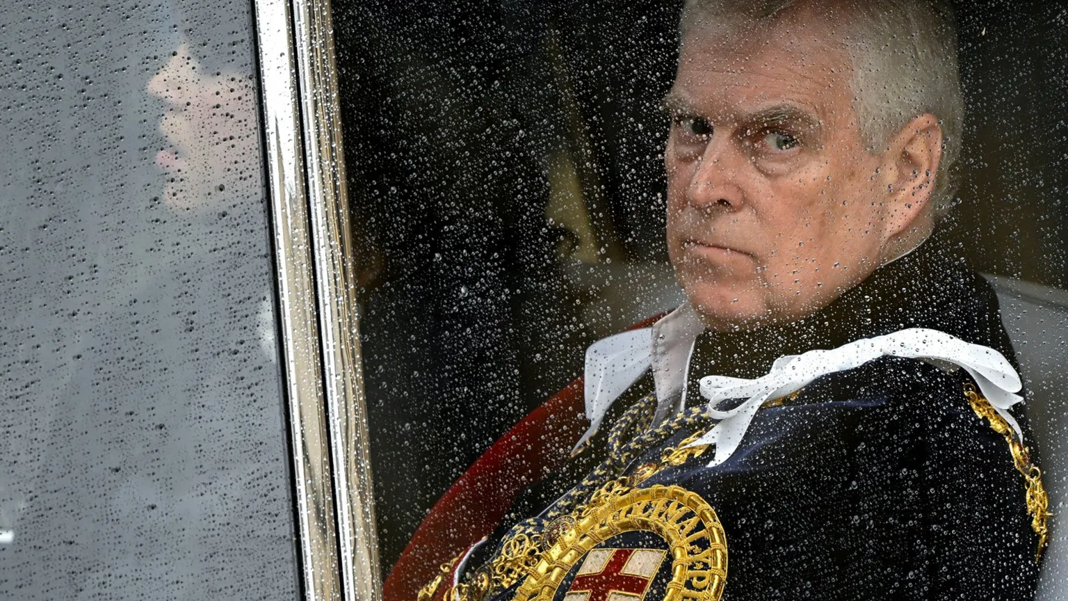 Prince Andrew looking somber while sitting in a car, wearing royal uniform with golden trim and St George's cross, photographed through rain-spotted car window glass during recent public scrutiny over his associations with Jeffrey Epstein and subsequent removal of royal titles