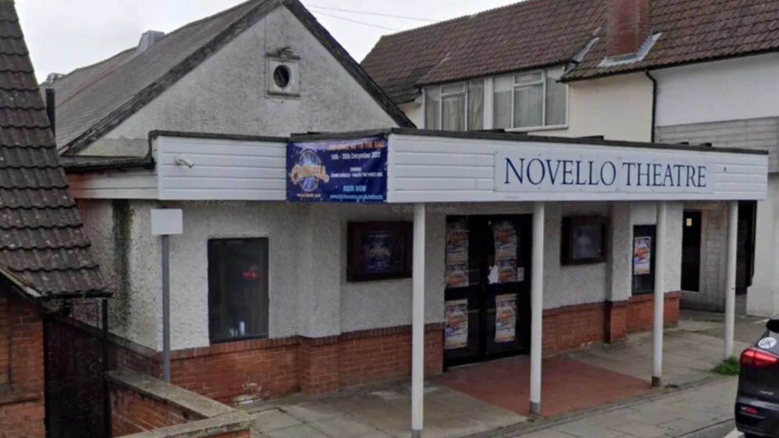 Exterior of the Novello. A white rendered building with a pitch roof and a covered entrance supported by small pillars that extends over the pavement