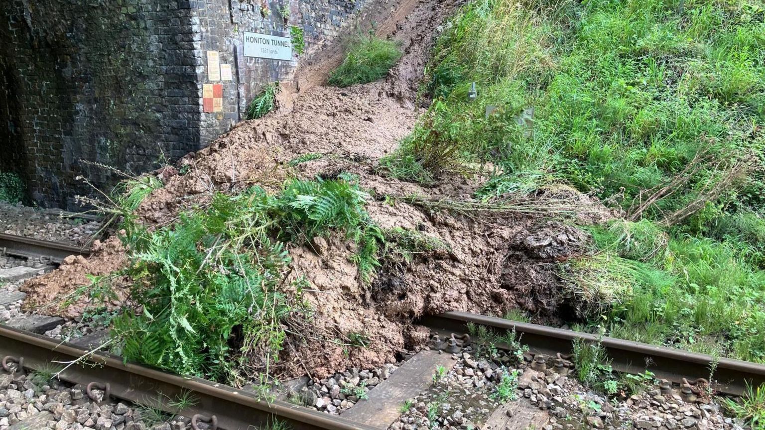 Blocked train line between Axminster and Honiton. A large amount of mud and debris is on the line in front of a tunnel