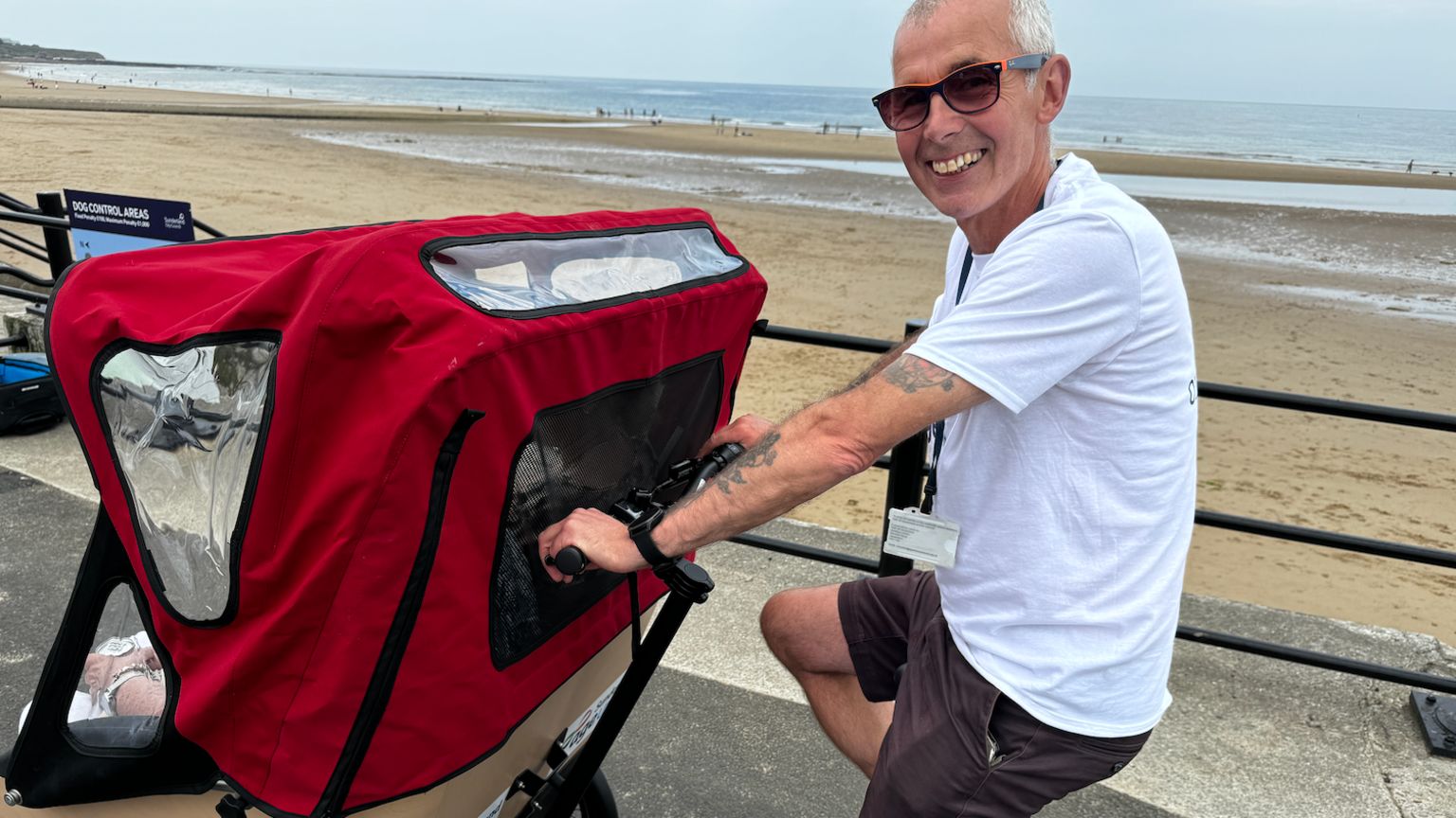 Colin Thompson, wearing a white t-shirt and black shorts, pushing a red trishaw on Seaburn seafront.