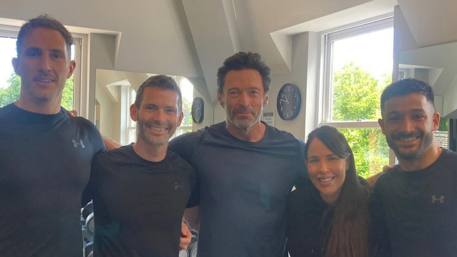 A group picture of gym staff with Hugh Jackman in the middle. they are all wearing black t-shirts.