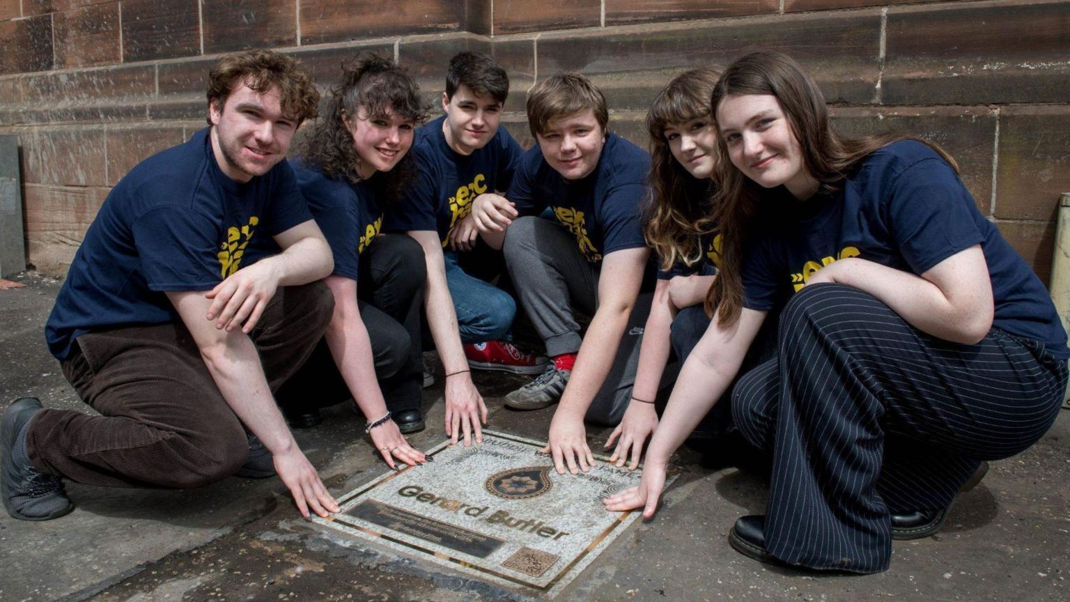 A group of theatre students touching Gerard Butler's marble plaque on the ground