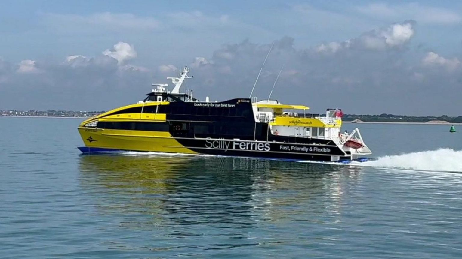 The Atlantic Wolff, a yellow and black ferry, moving over the water to the left of the picture with the white wake visible behind