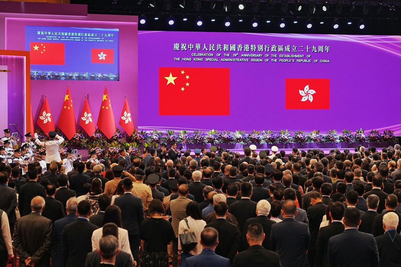 2026年7月1日，在香港湾仔的香港会议展览中心，现场举办庆祝香港成立29周年活动。多人站着背向镜头，眼望前方的中国国旗及特区区旗。