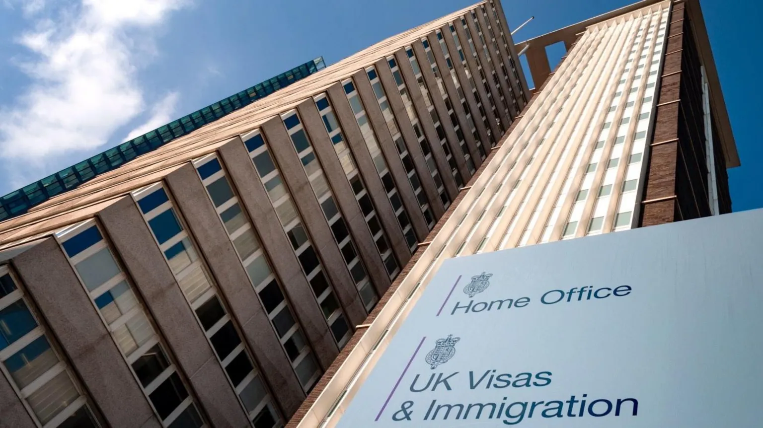 A tall rise building with a sign in front of it saying 'Home Office' and 'UK Visas & Immigration'