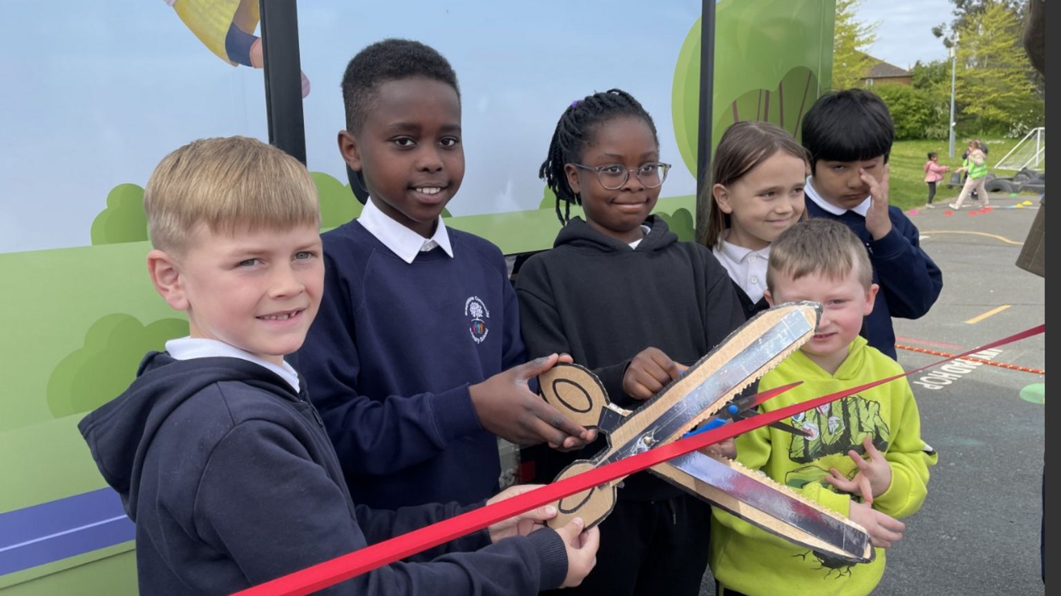 6 children help hold scissors to cut the red ribbon on the new book bus 