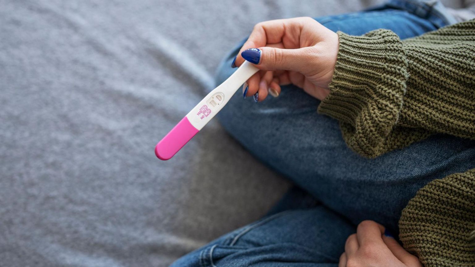 A close up of a woman holding a pink and white pregnancy test