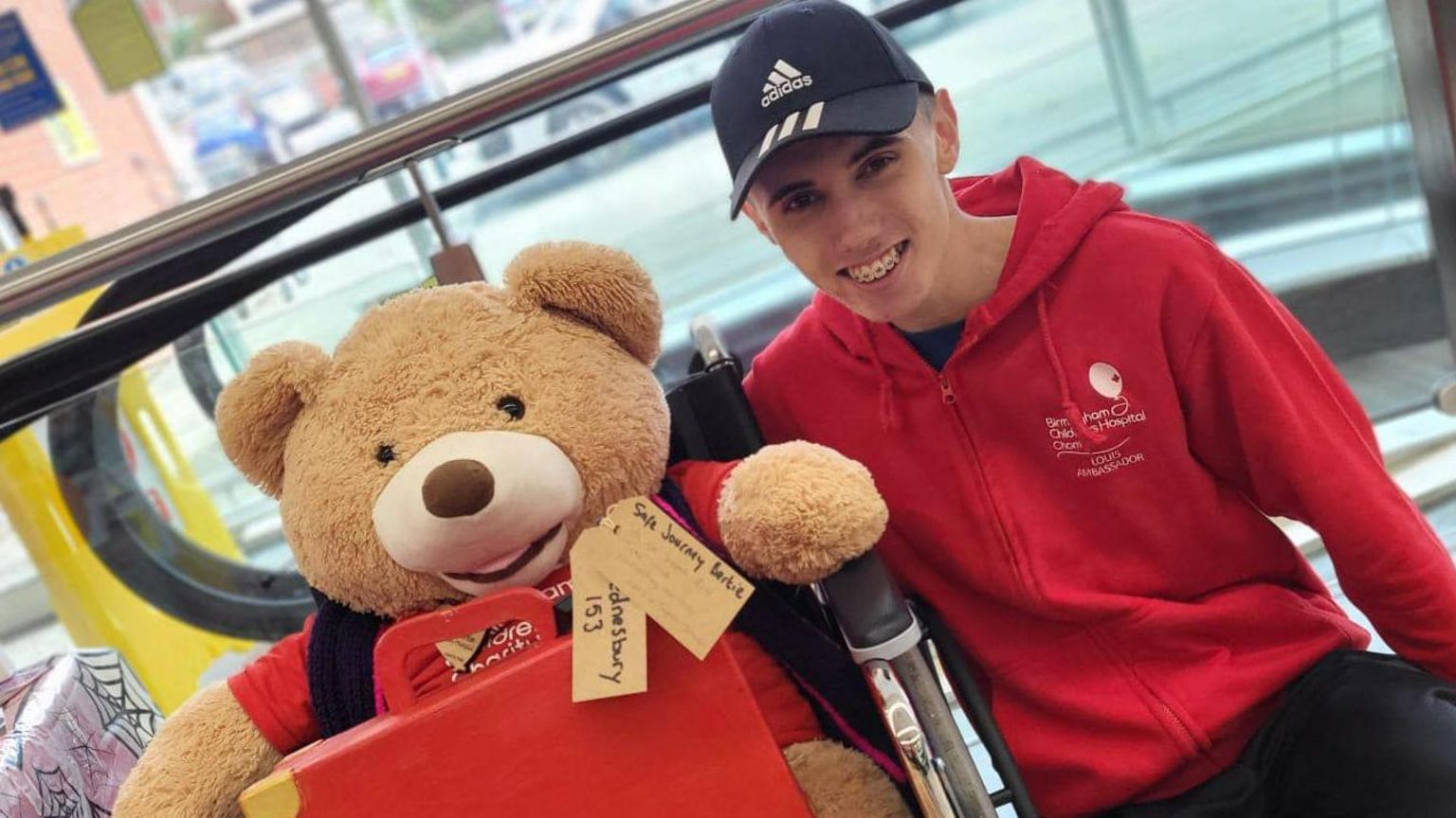 Louis in a Birmingham Children's Hospital hoodie next to a hospital teddy bear in a wheelchair