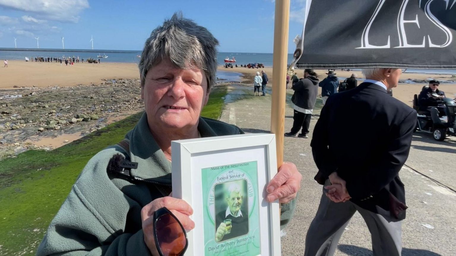 Elizabeth Brook holding a portrait of her father on Redcar seafront