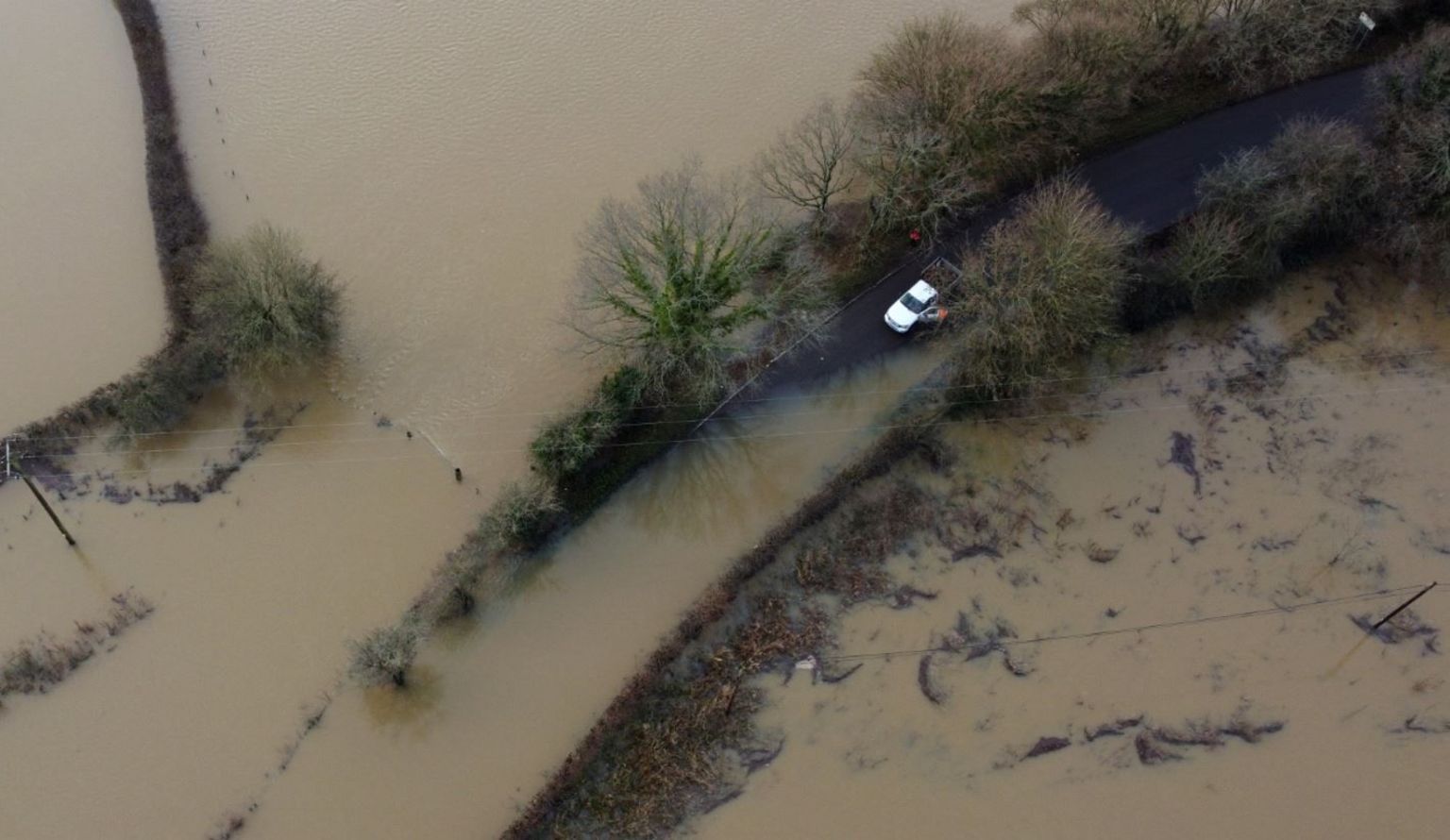 An aerial image of a white van parked beside a vast amount of muddy floodwater covering a road and fields either side of the carriageway
