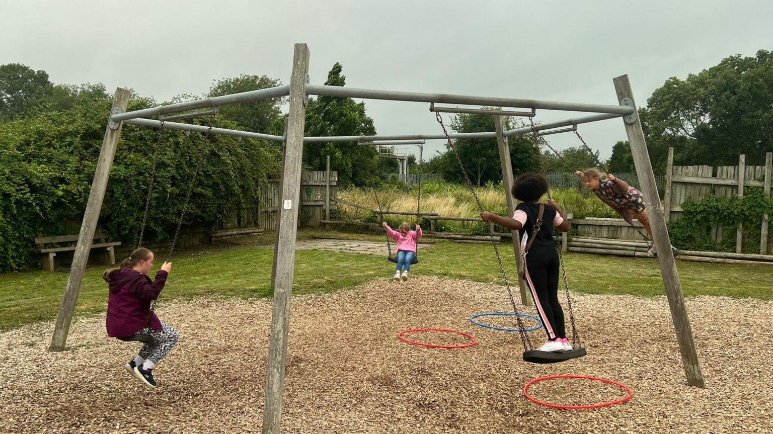 Four children playing on swings set in a circle on a timber frame outside