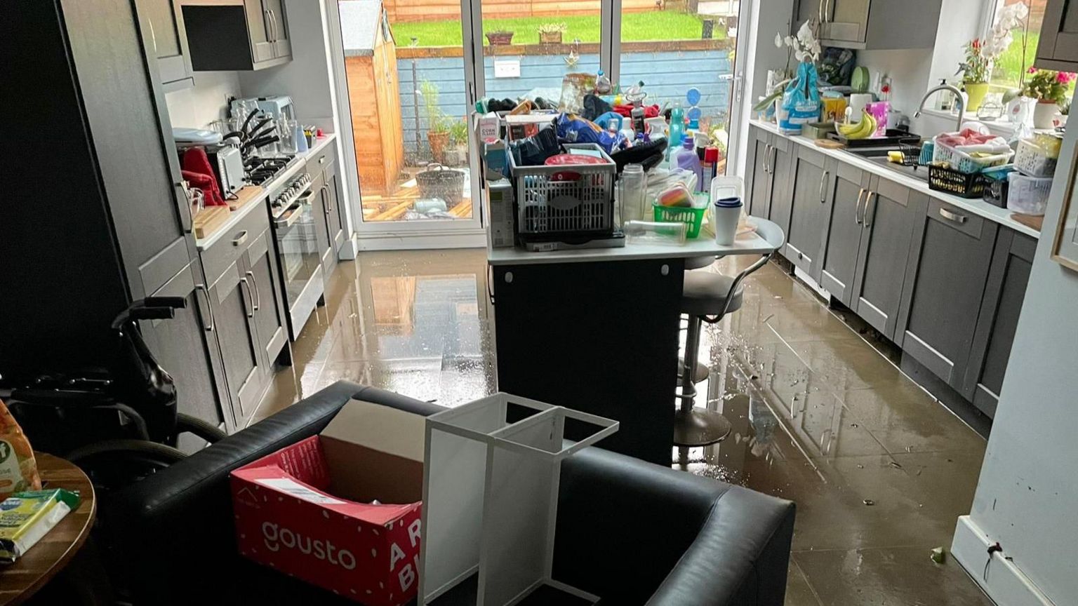 A kitchen floor is covered in water while items are stacked up high on a breakfast bar