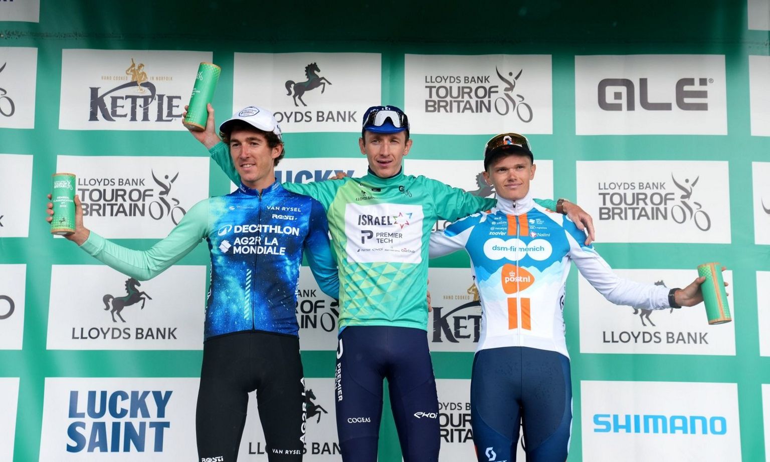 Three men standing on the podium wearing cycling lycra with sponsorship names on