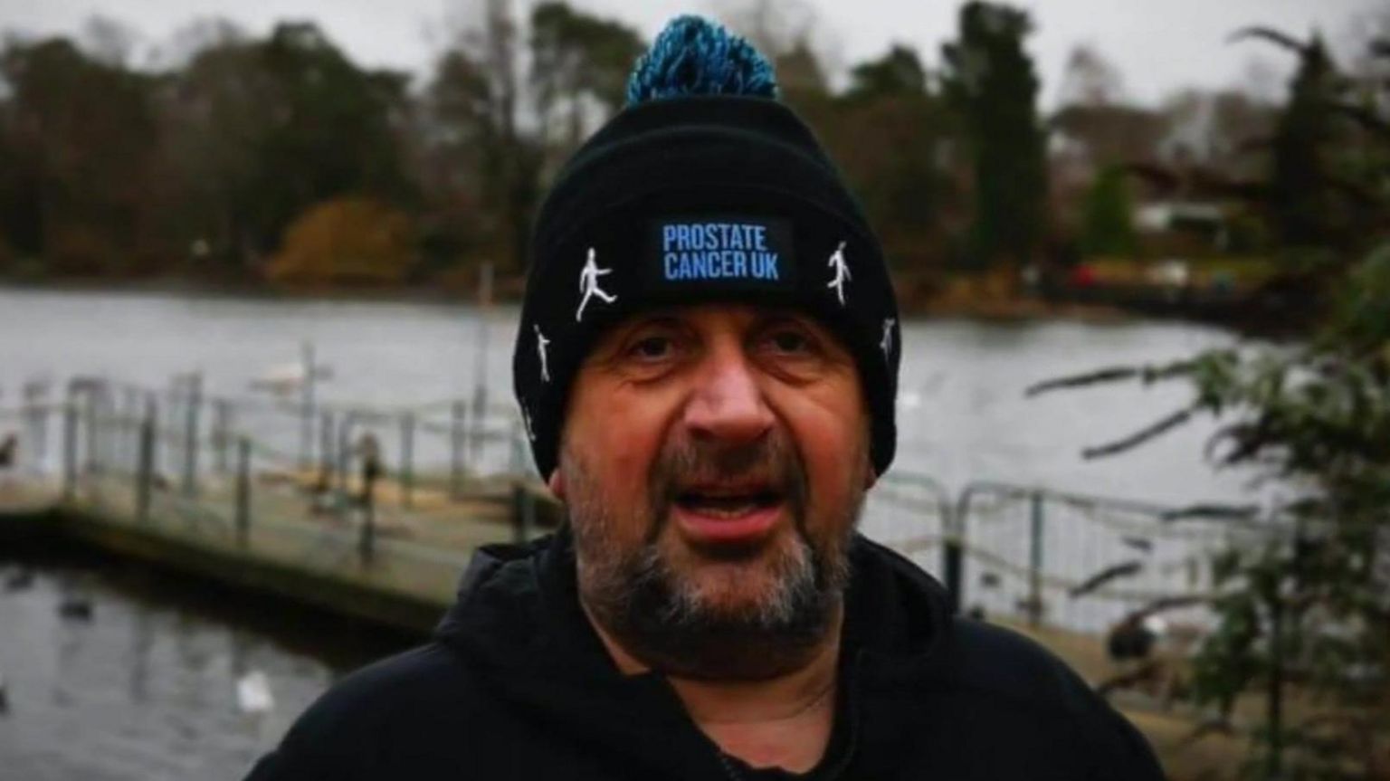 Kevan Birkett, a man with a beard wearing a beanie hat which reads "prostate cancer UK"