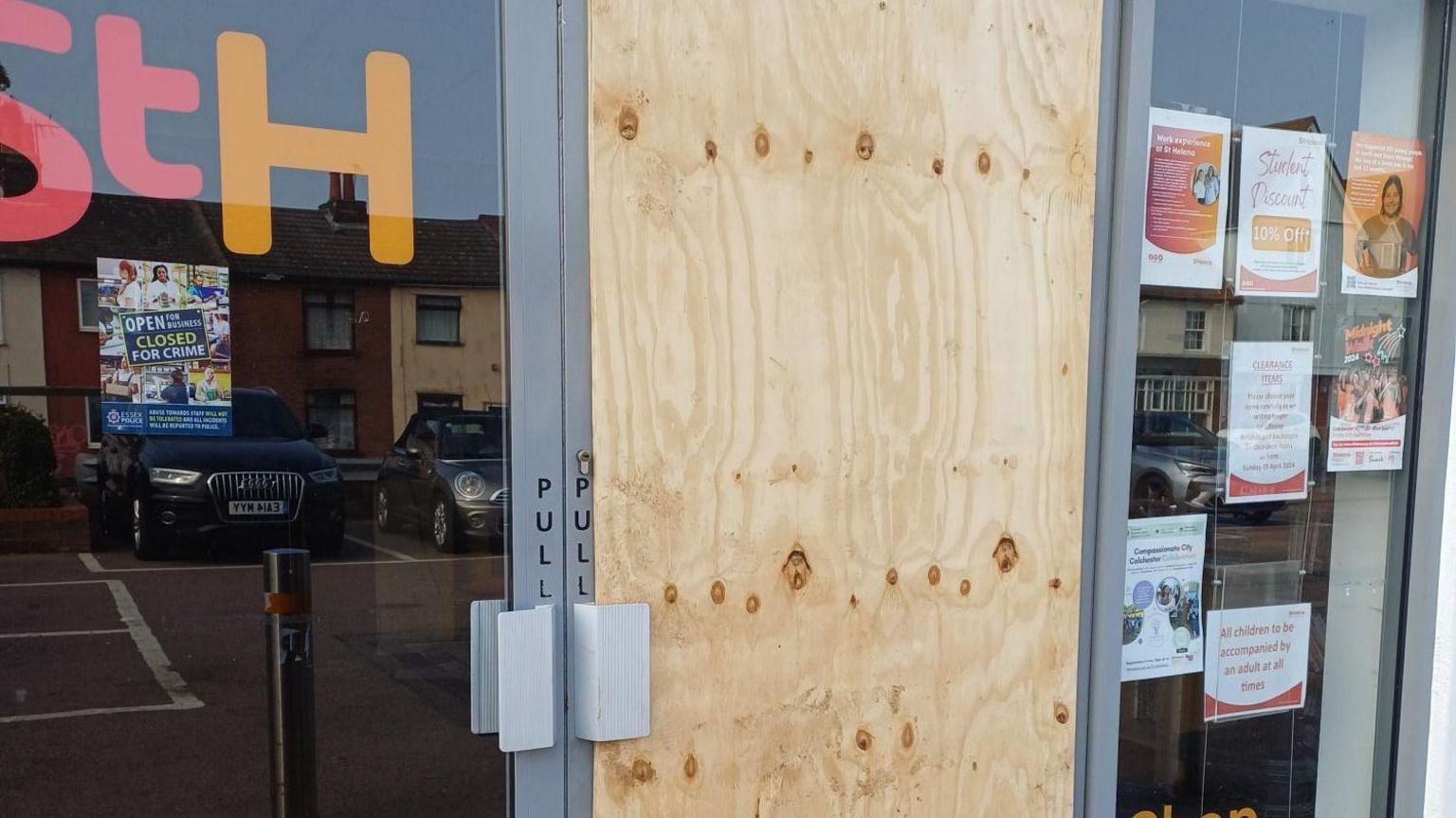 A boarded up glass door outside a charity shop