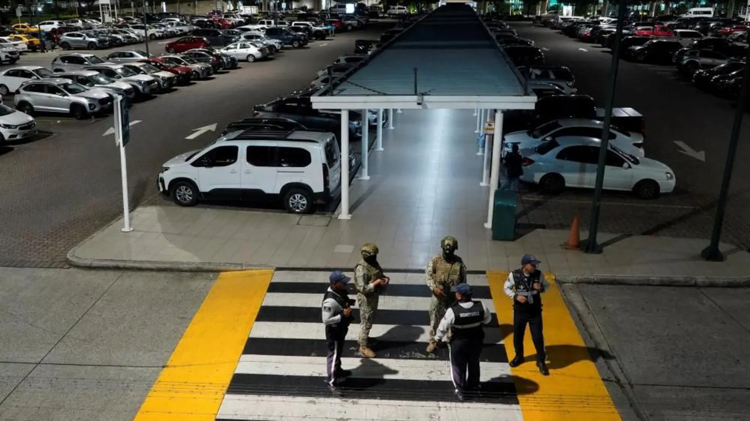 REUTERS/Cesar Munoz Members of Ecuador's armed forces stand stand guard after an armed attack at the airport in Guayaquil. There are two soldiers with guns and three other uniformed men standing on a pedestrian crossing leading to the parking lot.