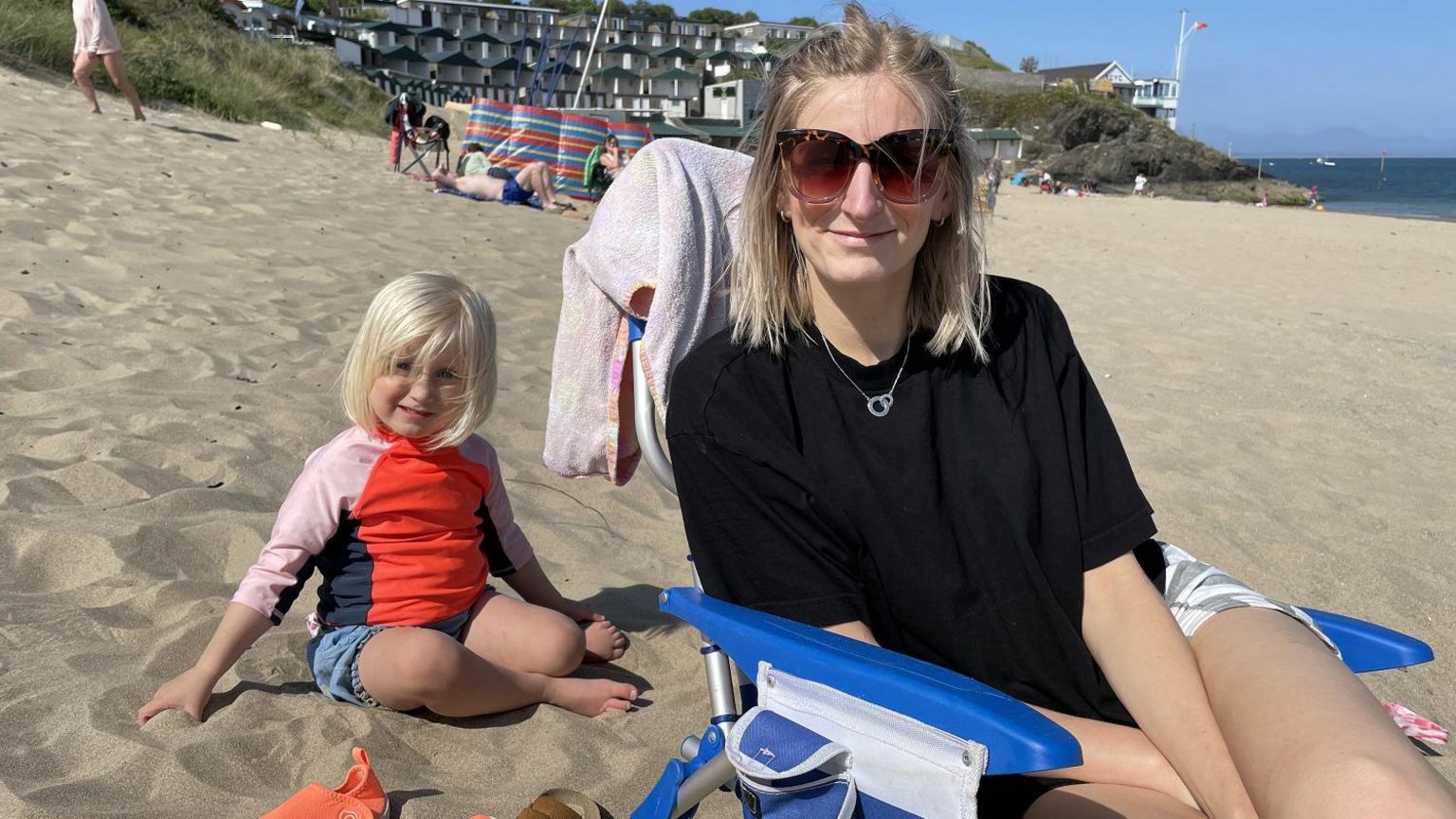 Grace Earnshaw sat in a camping chair on the beach at Abersoch, wearing sunglasses, with her young daughter sat beside her on the sand