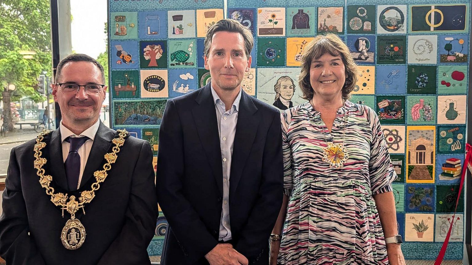 Two men and a woman standing in front of a blue patchwork quilt