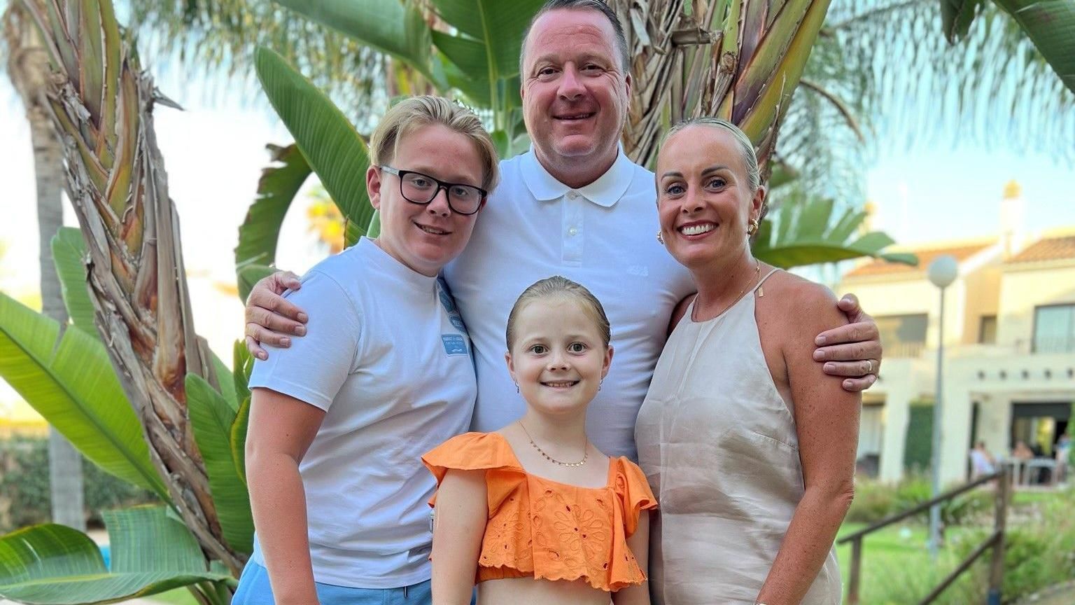 Family photo of two children and parents in front of a palm tree