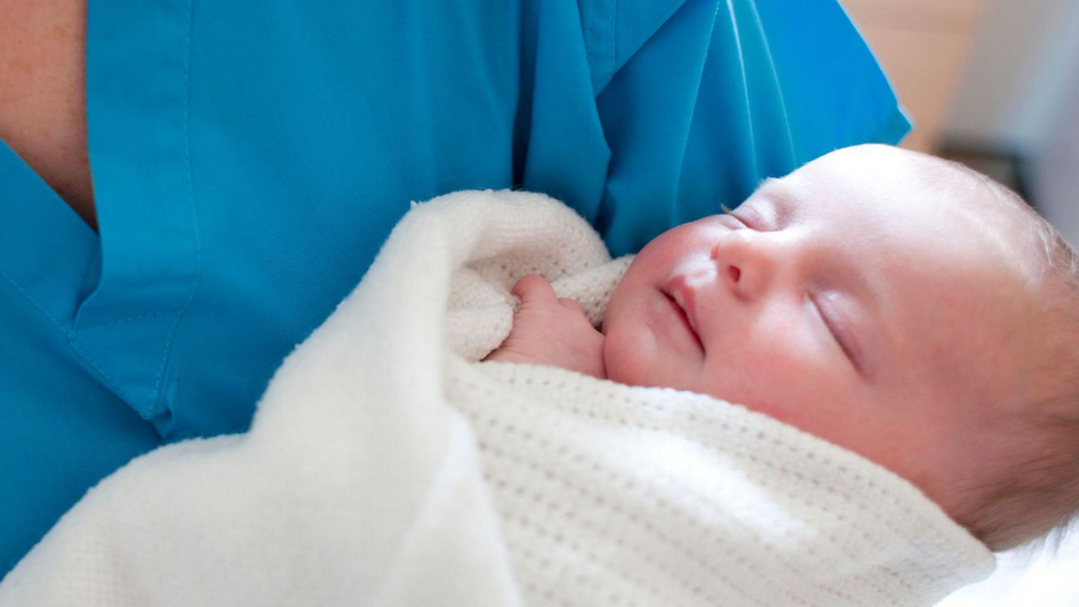 Midwife in scrubs holds sleeping baby in blanker