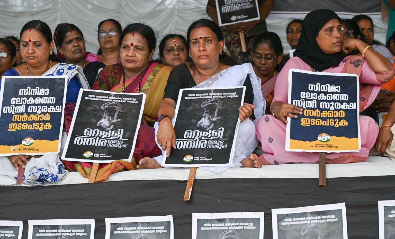 Women from the Mahila Congress sit in protest, holding up posters,  demanding action on Hema panel report in Kochi on Friday