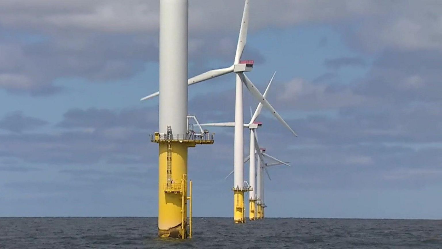 White wind farm turbines with yellow bottoms in the sea on a cloudy day.