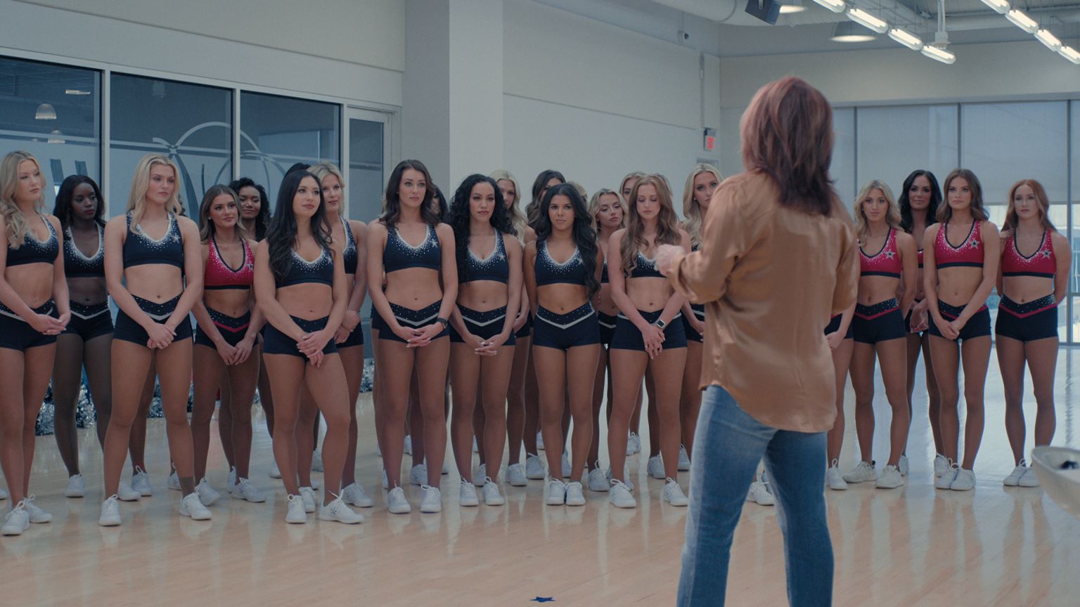 A large group of cheerleaders standing in a row, with their coach in front speaking to them