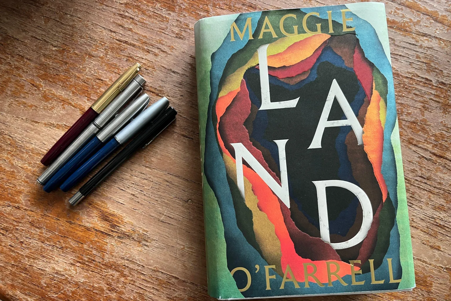 BBC/Katie Razzall 5 fountain pens on the left and copy of her new book Land on the right
front cover has bright colours of red, orange, blue and green